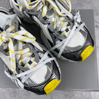 Gray and black chunky sneakers with white laces and yellow heel accents on box.