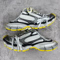 Gray and black chunky sneakers with white laces and yellow trim, unisex style.
