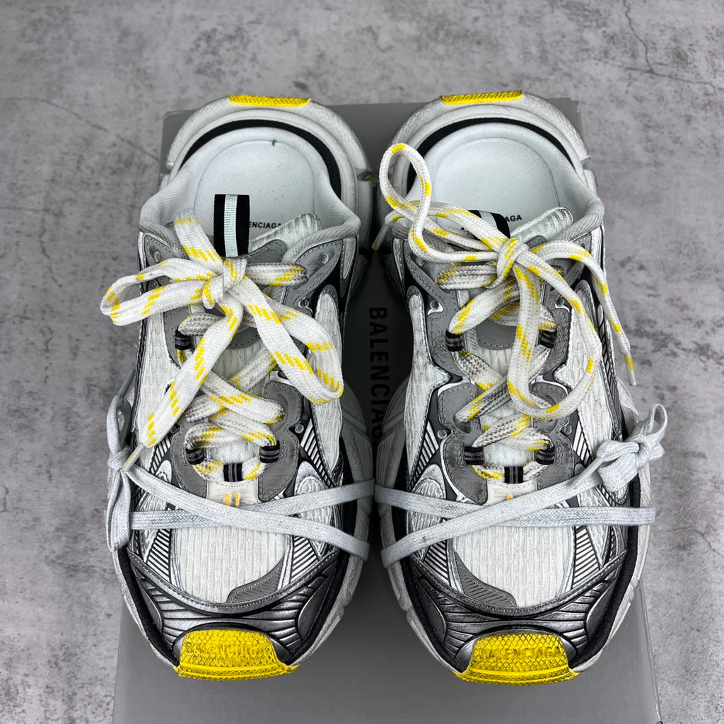 Gray and black chunky sneakers with white laces, yellow heel tabs, Balenciaga on tongue.