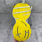 Shoe outsole of gray chunky sneakers with bright yellow tread and ridges.