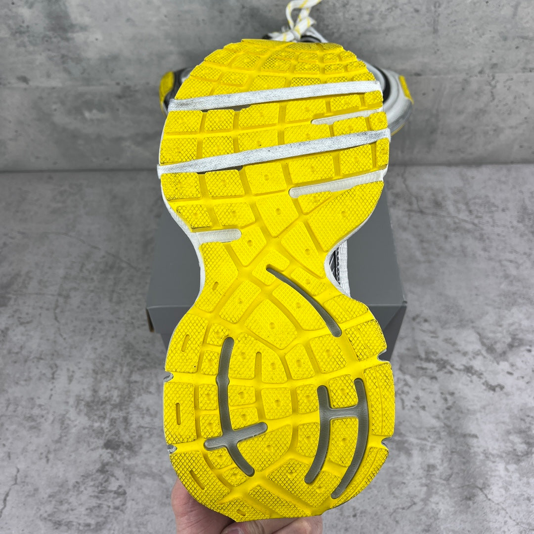 Shoe outsole of gray chunky sneakers with bright yellow tread and ridges.