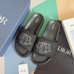 Black slide sandals with wide fabric strap featuring white DIOR monogram, pair on box