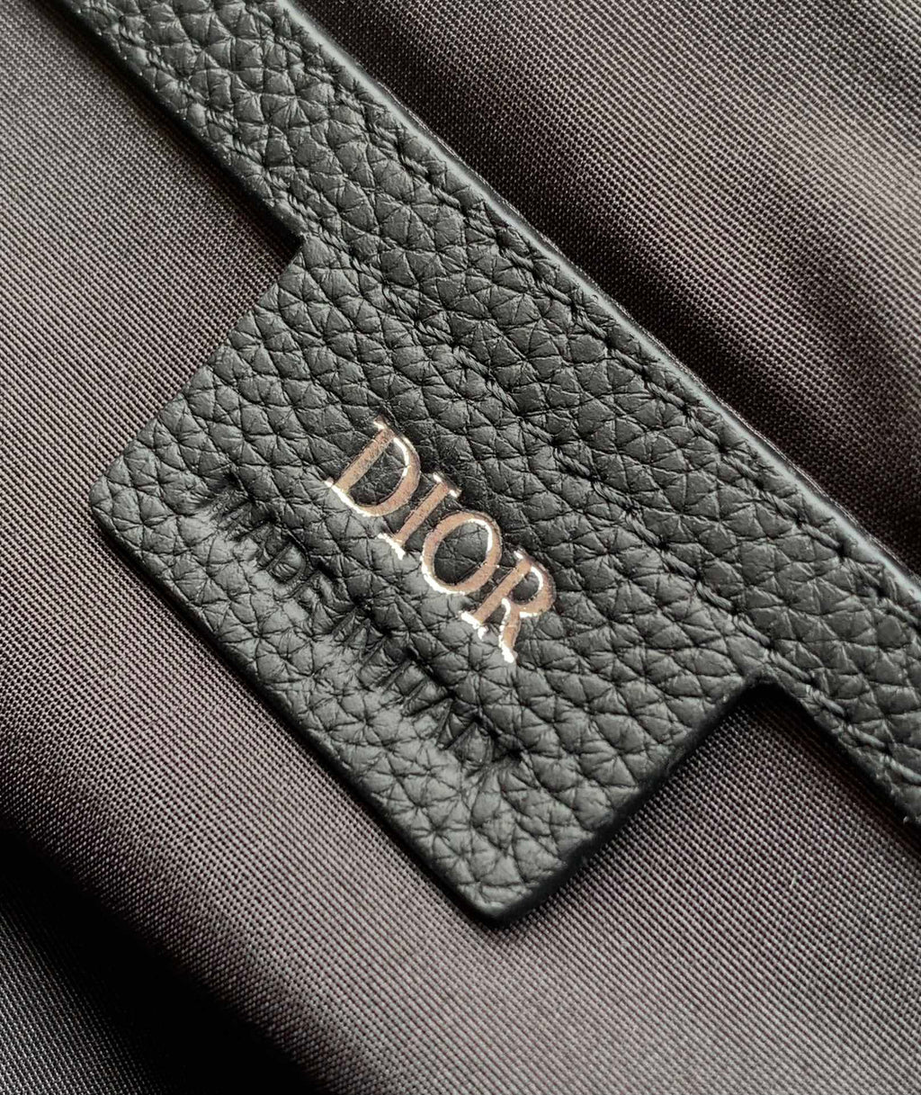 Dior bag logo patch close-up on dark leather with embroidered stitching.