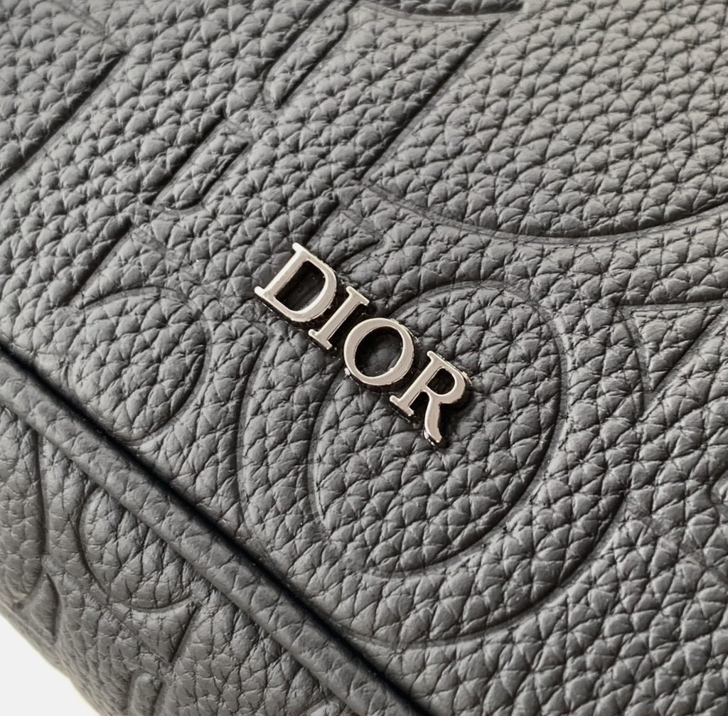 Dior bag close-up of “DIOR” logo on textured dark leather flap.