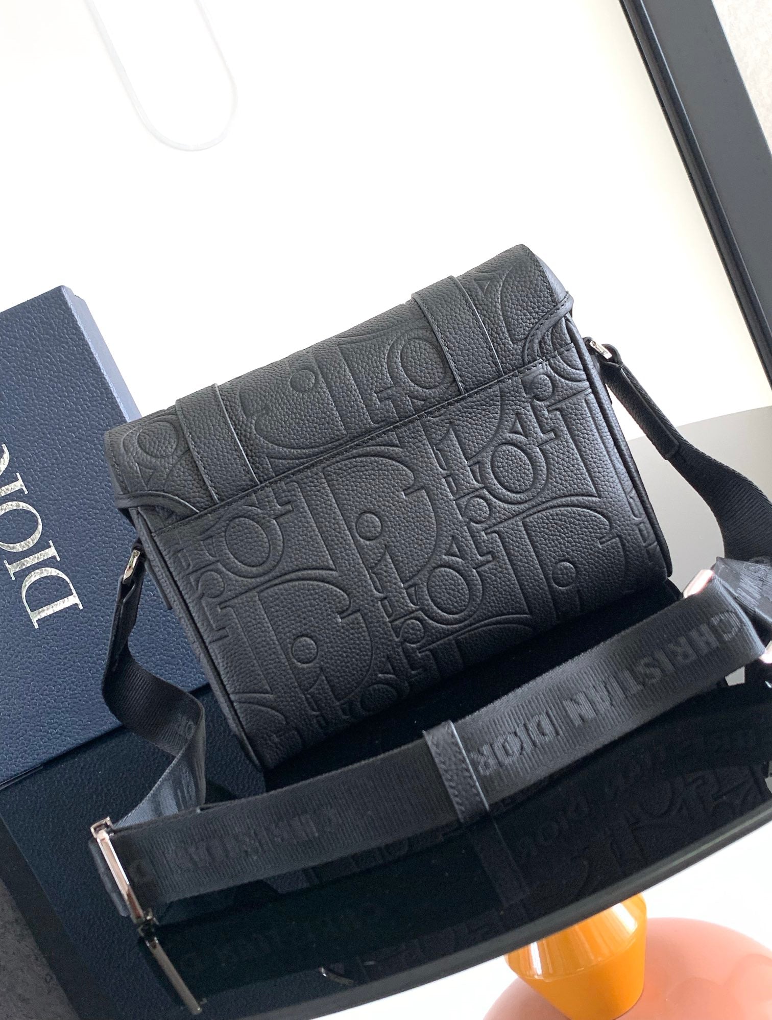 Dior bag with embossed monogram pattern and top flap with dark strap.