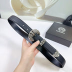 Dark leather belt with ornate oval buckle and decorative keeper, held at an angle