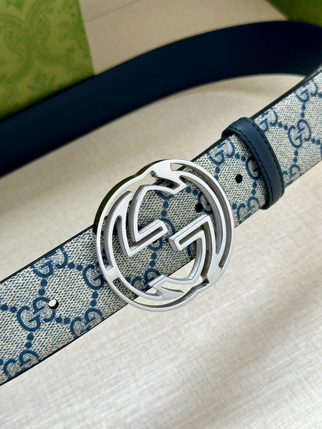 Gucci belt close-up: blue GG canvas strap with silver interlocking G buckle on dark blue leather