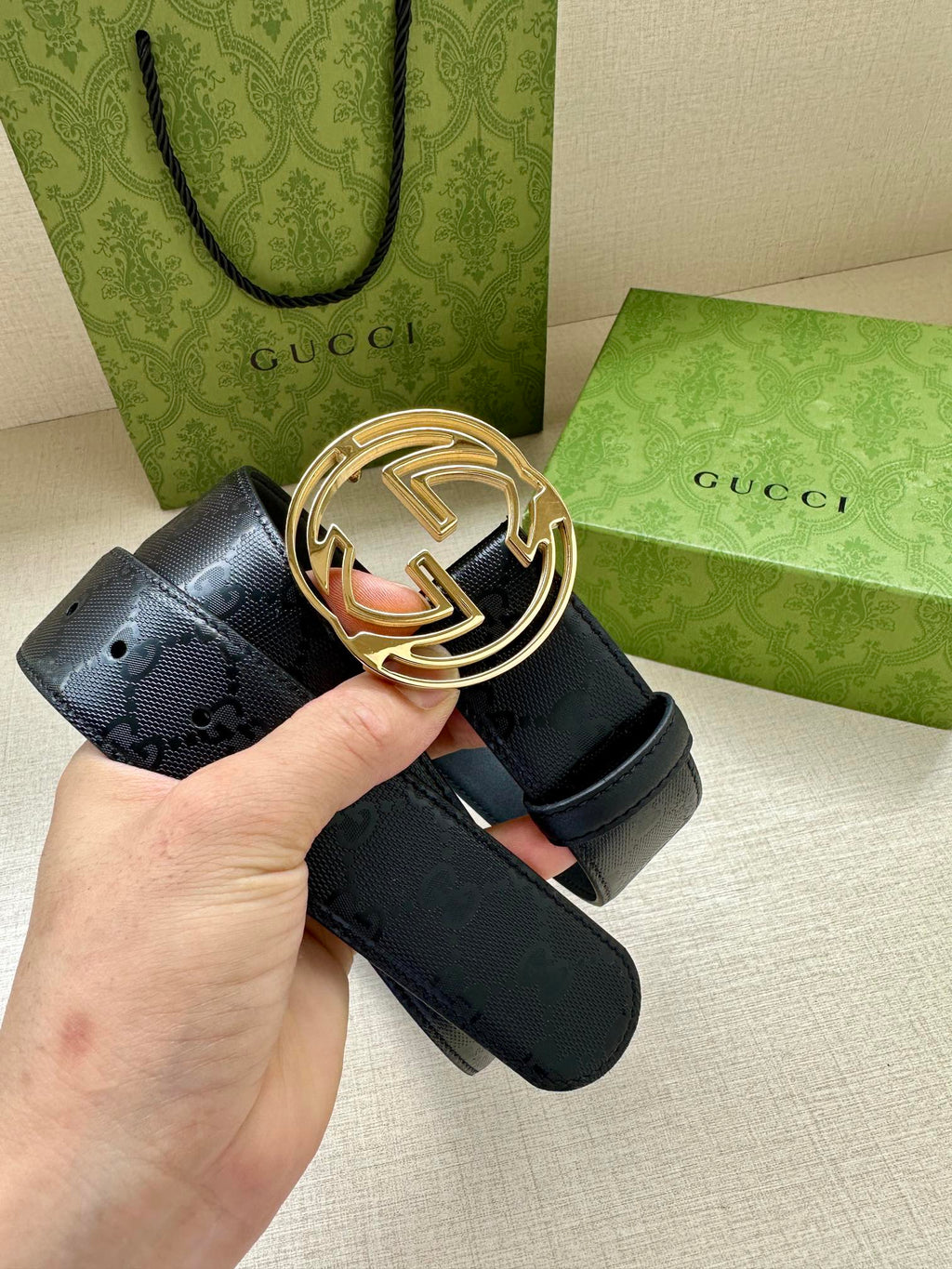 Gucci belt with dark blue strap and gold interlocking G buckle, held in hand.