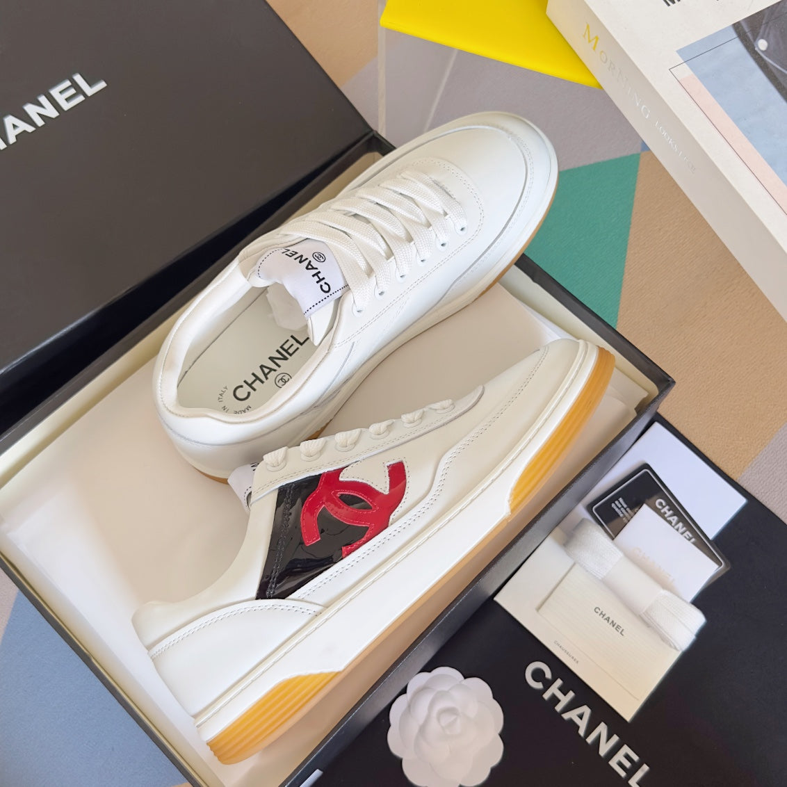 White low-top sneakers with red CC logo and lace-up uppers on shoe box