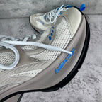 White sneaker with textured mesh, blue logo detail, and thick black outsole.