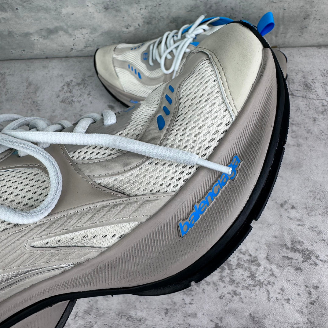 White sneaker with textured mesh, blue logo detail, and thick black outsole.
