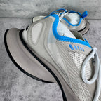 White mesh sneaker with blue trim, cushioned tongue, and thick black sole.