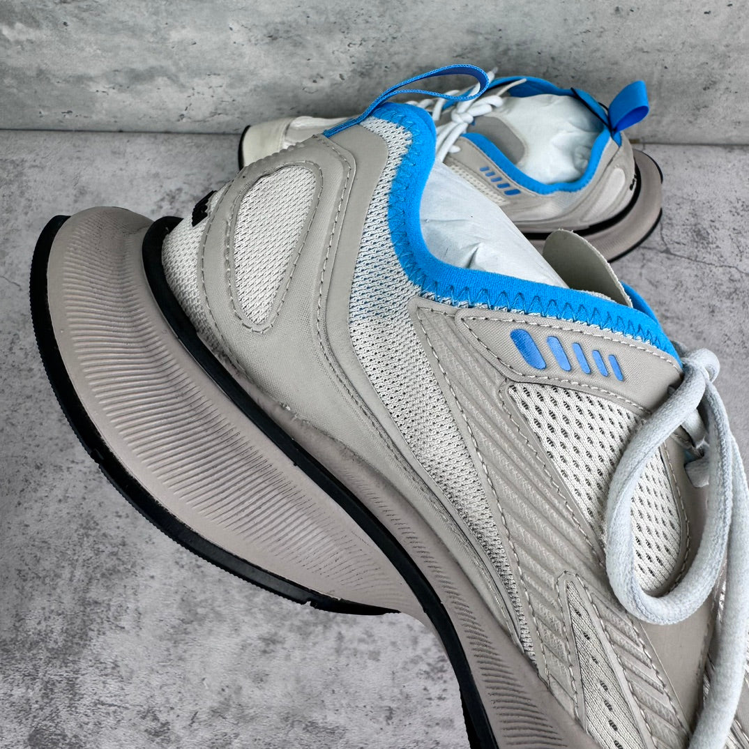 White mesh sneaker with blue trim, cushioned tongue, and thick black sole.