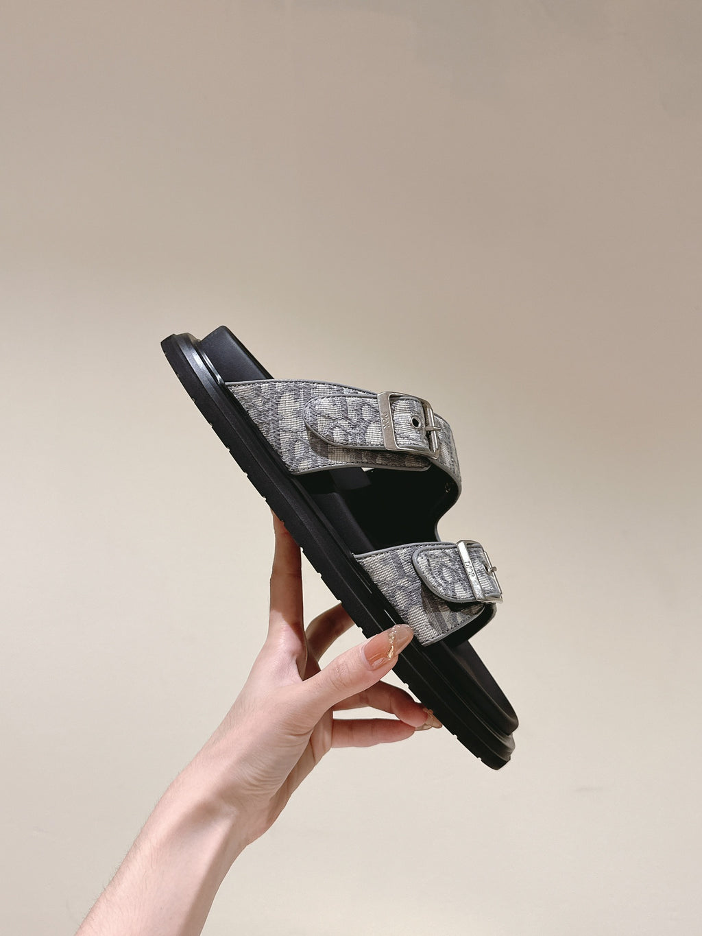 Dior slide sandals held at angle, monogram strap with metal buckles and black sole