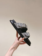 Dior slide sandals held at angle, monogram strap with metal buckles and black sole