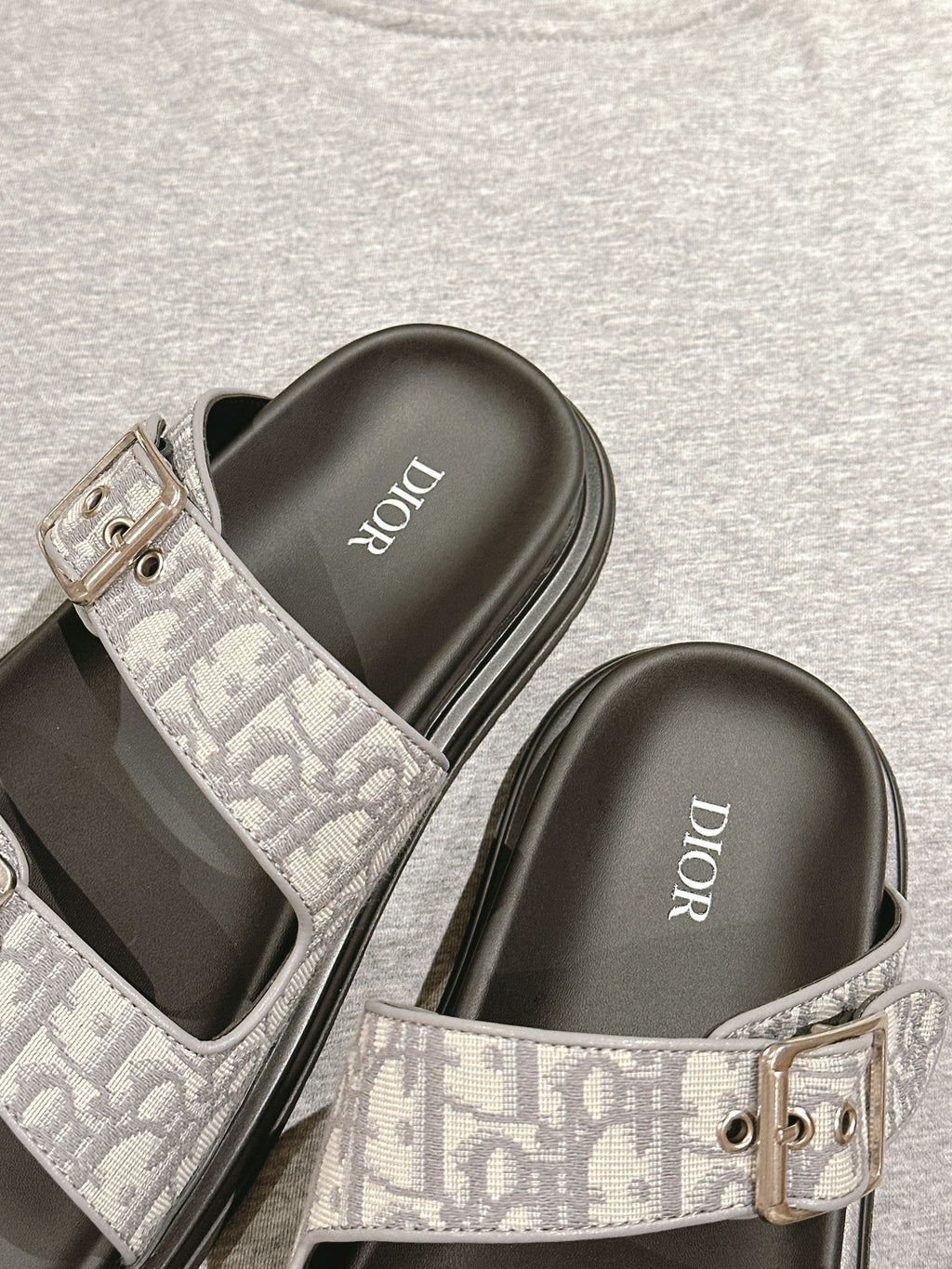 Dior slide sandals close-up: gray monogram strap with metal buckle over black footbed