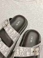 Dior slide sandals close-up: gray monogram strap with metal buckle over black footbed