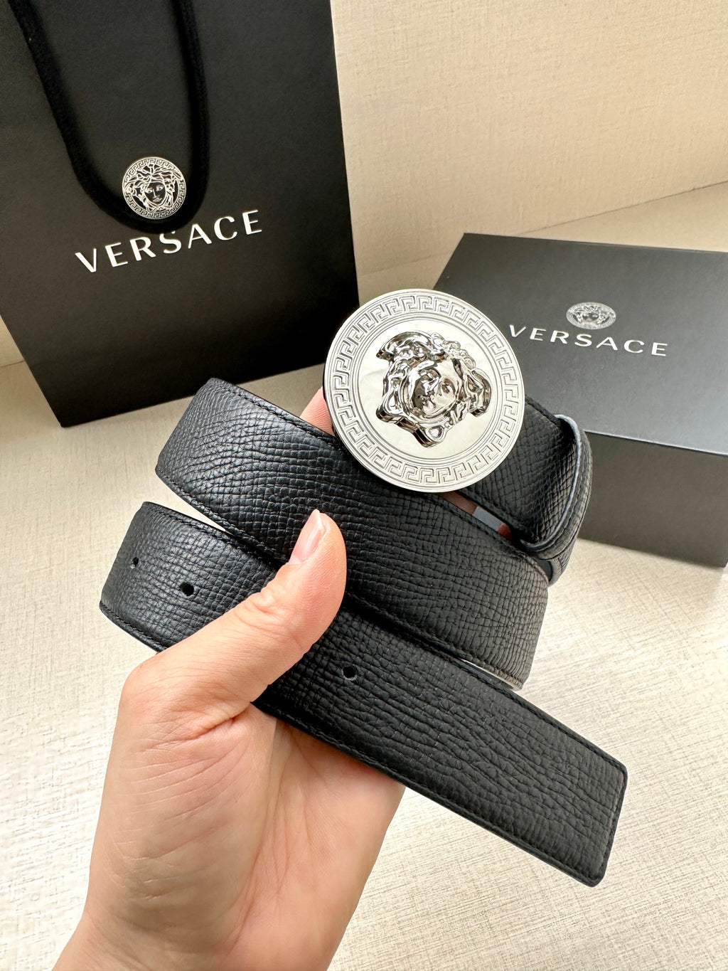 Dark leather belt with round silver Medusa buckle held in hand