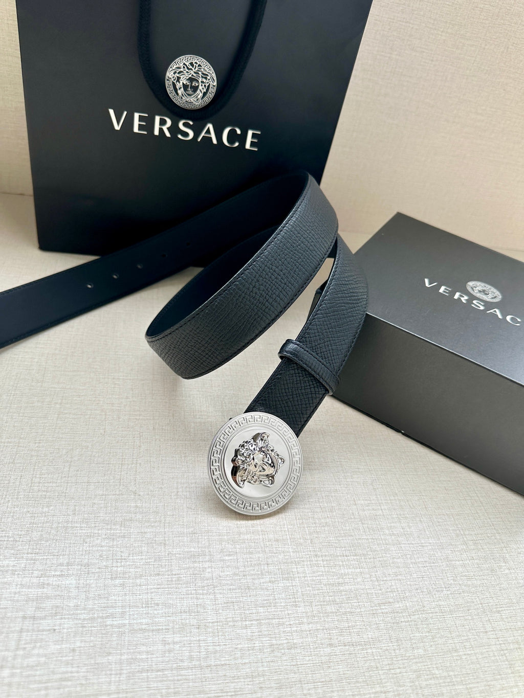 Dark leather belt with round silver Medusa buckle and keeper strap