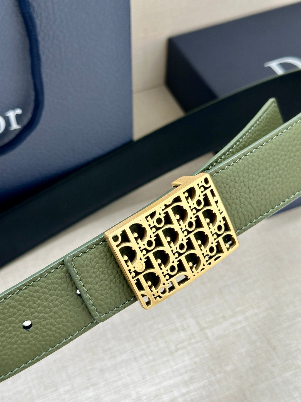 Dior belt close-up: olive strap with gold square buckle featuring Dior monogram