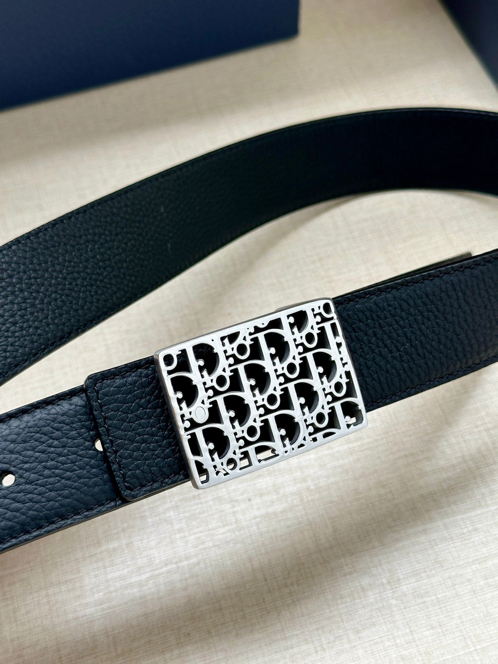 Dior belt close-up: dark leather strap with square monogram buckle detail.
