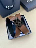 Reversible leather belt in box: brown strap and silver-toned Dior-pattern buckle on top.