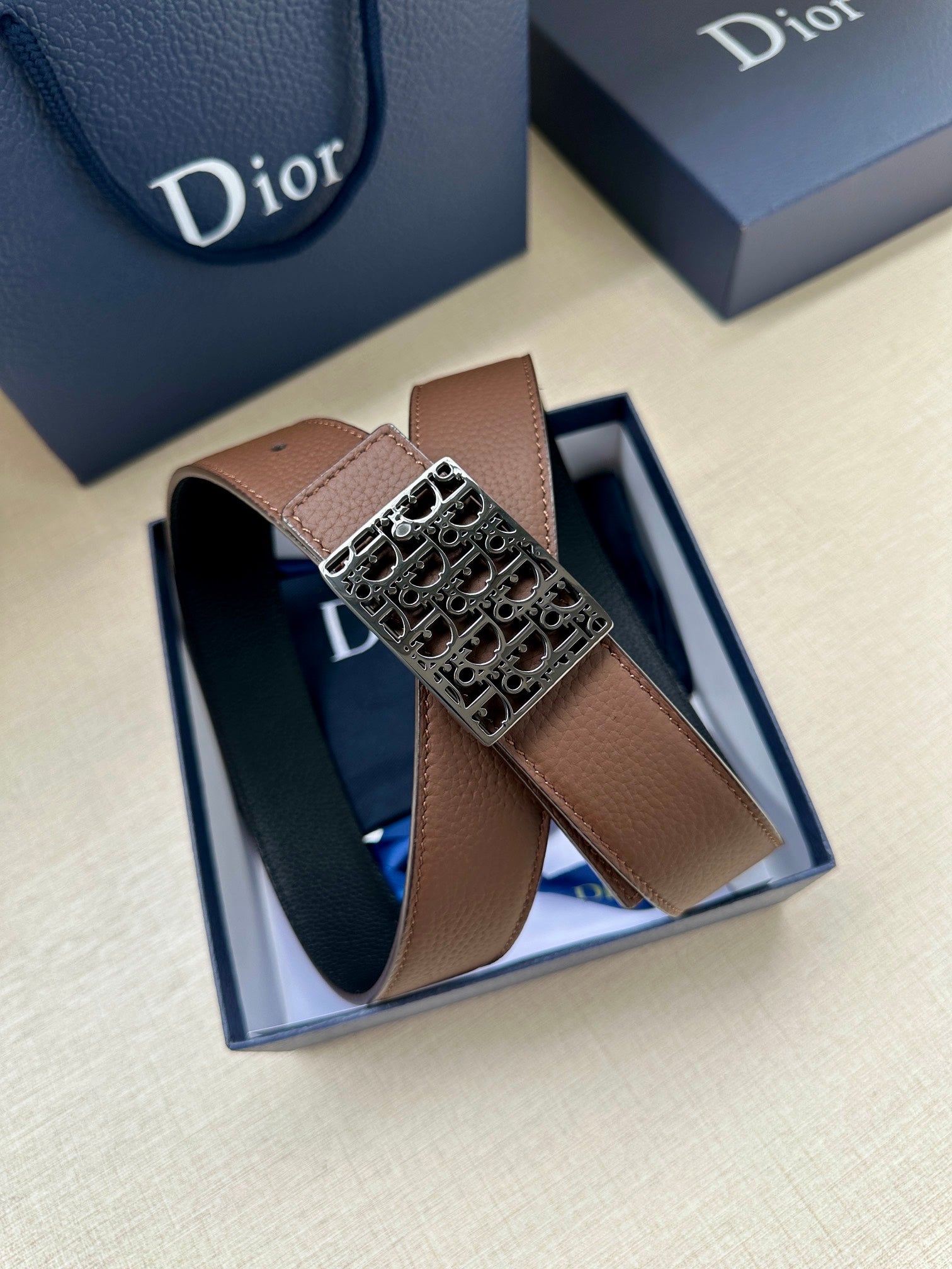 Reversible leather belt in box: brown strap and silver-toned Dior-pattern buckle on top.