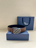 Reversible leather belt with brown strap and silver-toned Dior-pattern buckle, on blue gift box.