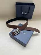 Reversible leather belt with brown strap and silver-toned Dior-pattern buckle, resting on gift box.