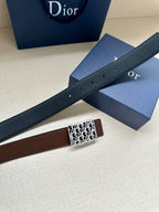 Reversible leather belt with dark strap and silver-toned Dior-pattern buckle, laid across boxes.