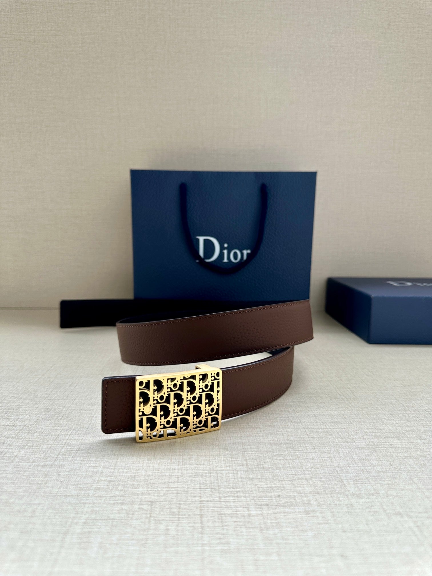 Reversible leather belt with gold Dior-pattern buckle and brown strap, shown at an angle.