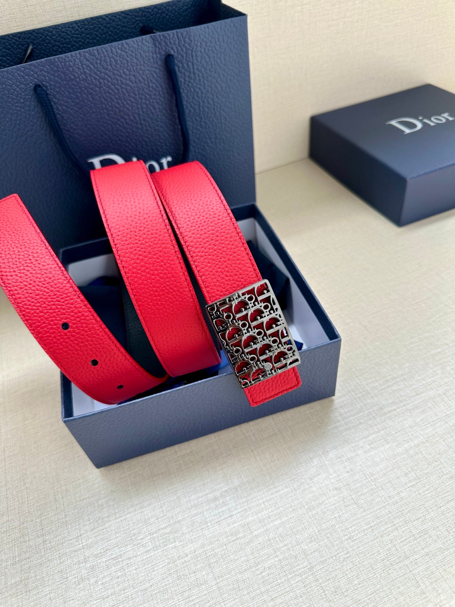 Dior belt set in red leather with dark strap and patterned buckle.