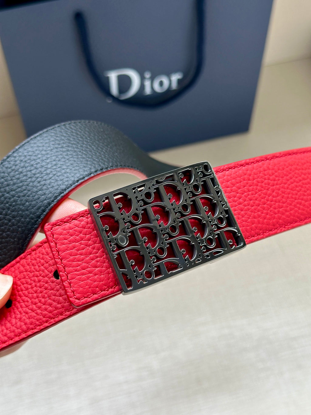 Dior belt close-up: red leather strap with textured black logo buckle.