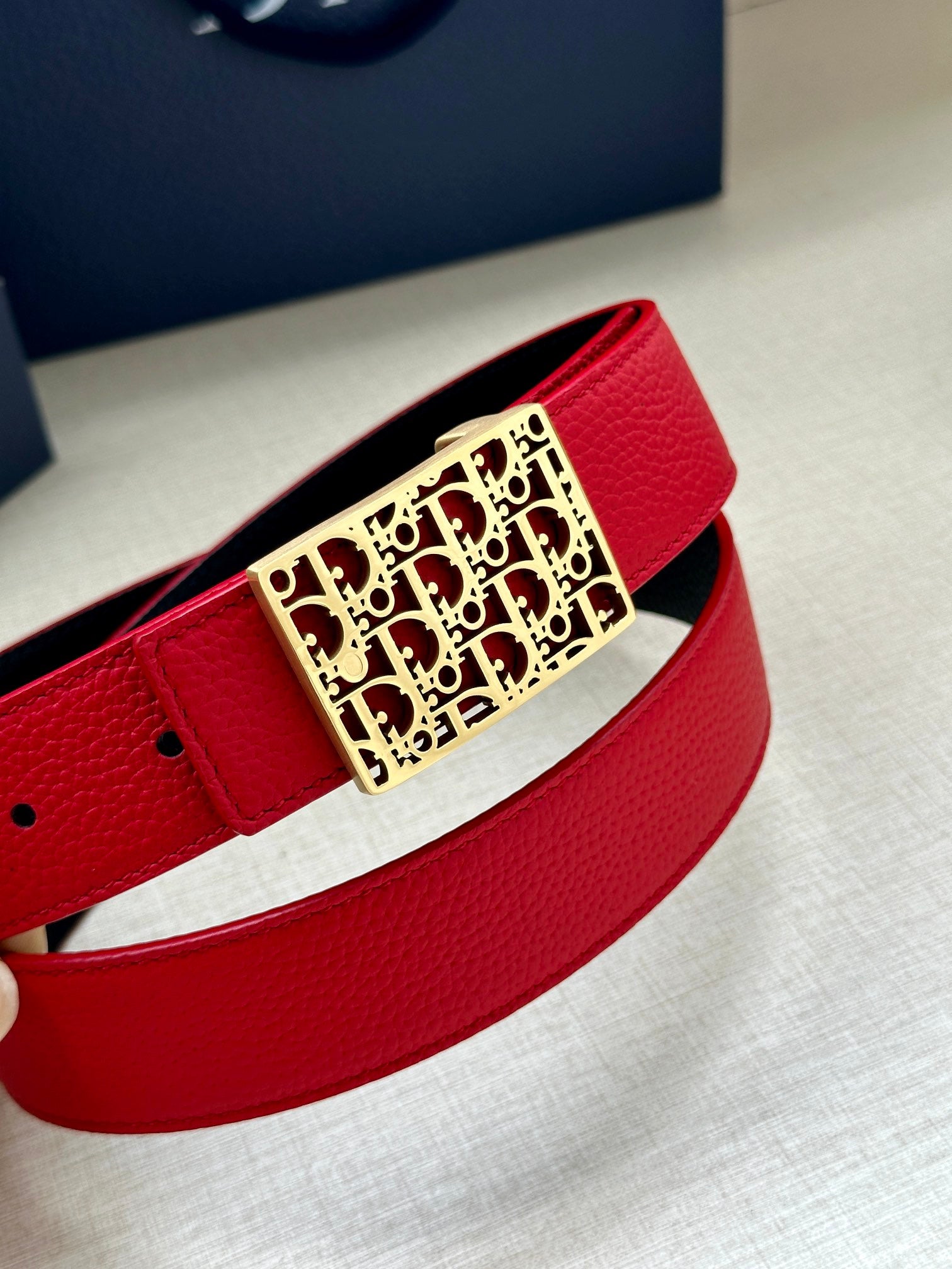 Dior belt close-up: red strap with gold-tone rectangular logo buckle.