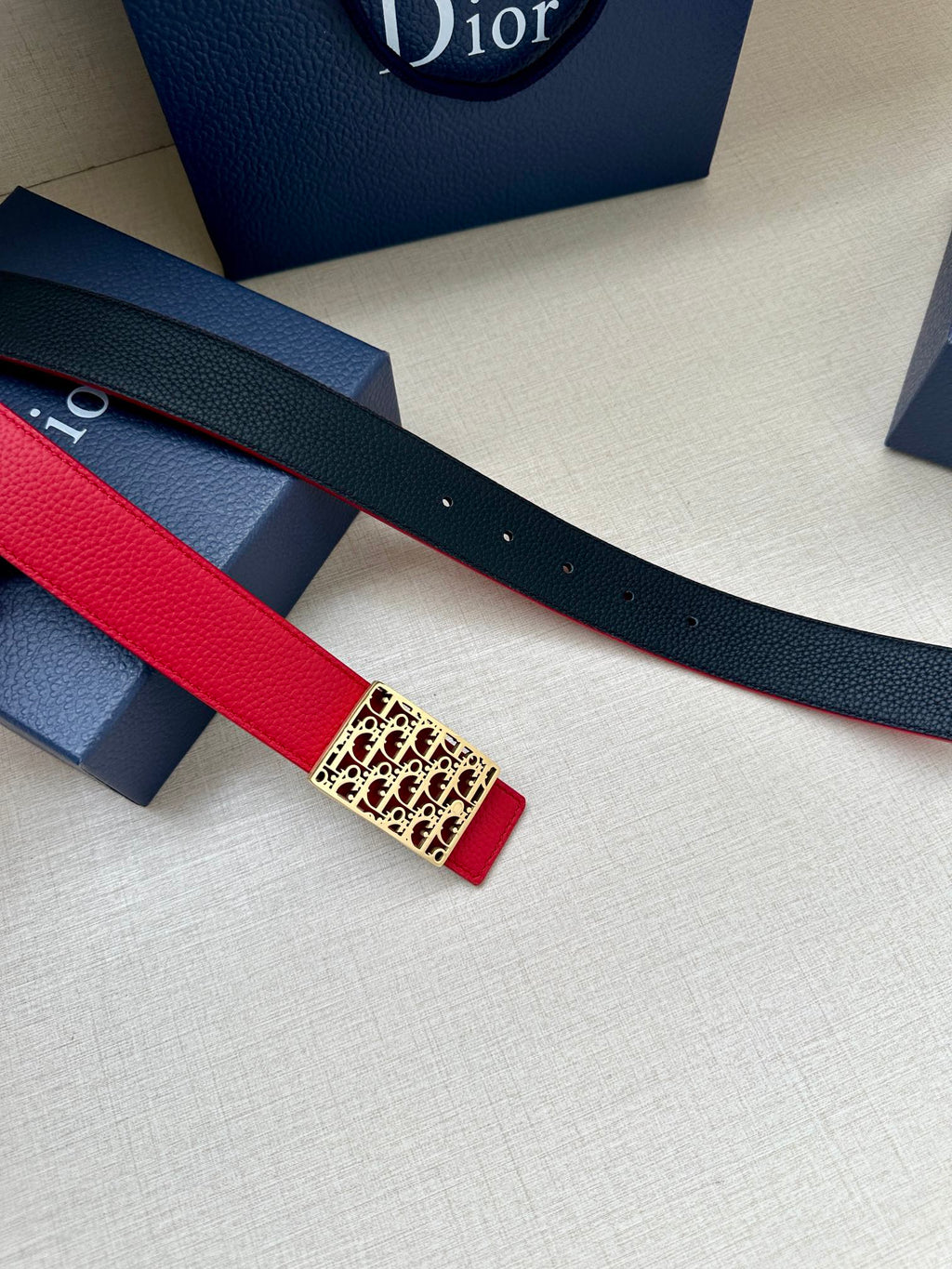Dior belt detail: red strap over navy backing with rectangular logo buckle.