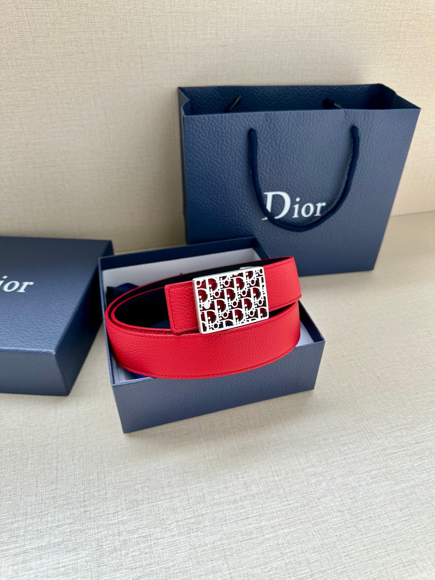Dior belt in red leather with patterned buckle and dual-tone strap.