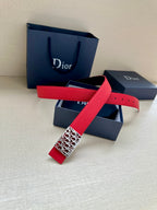 Dior belt with red strap and patterned rectangular logo buckle.