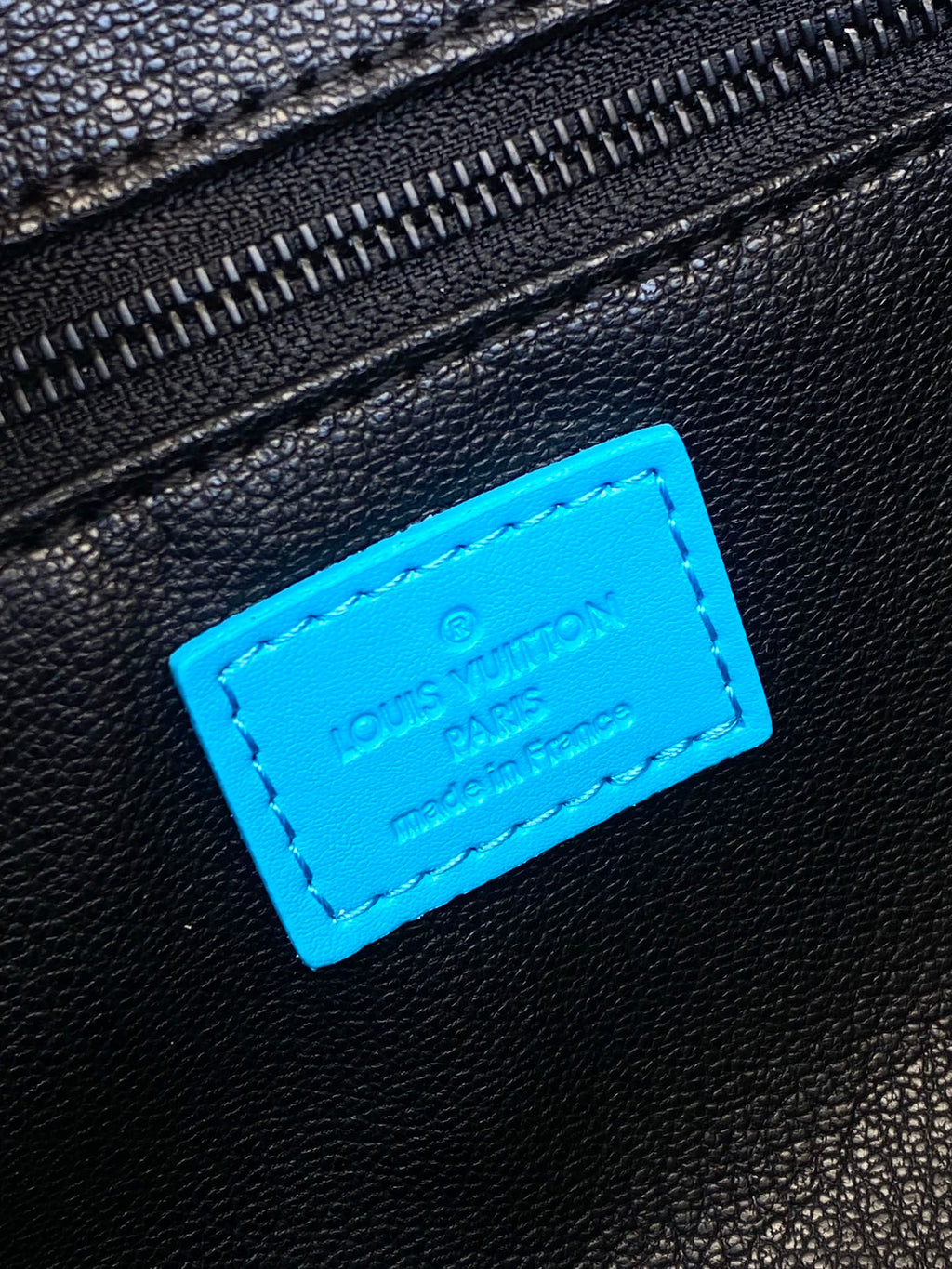 Louis Vuitton leather logo patch on black bag with bright blue stitched label