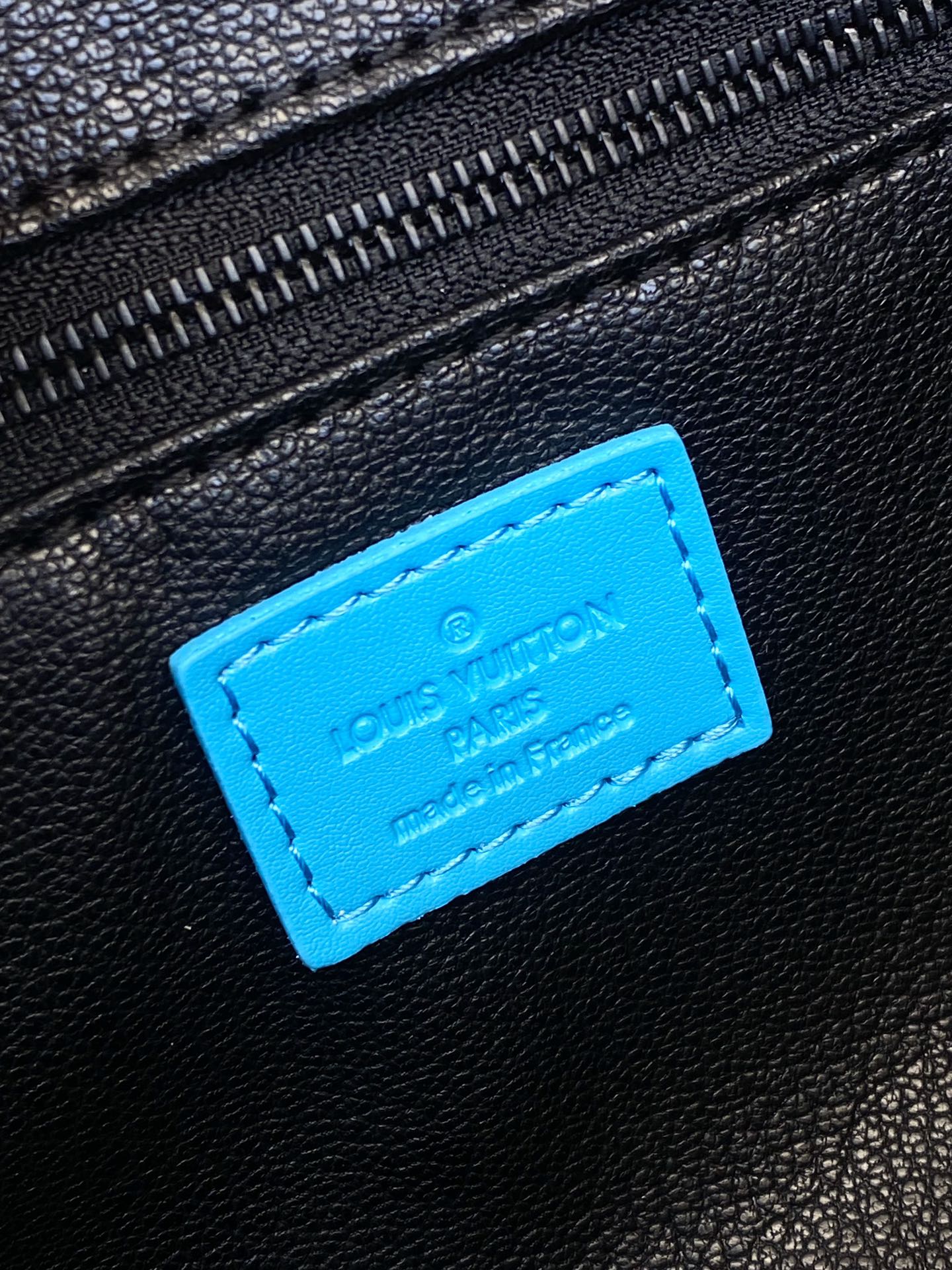 Louis Vuitton leather logo patch on black bag with bright blue stitched label