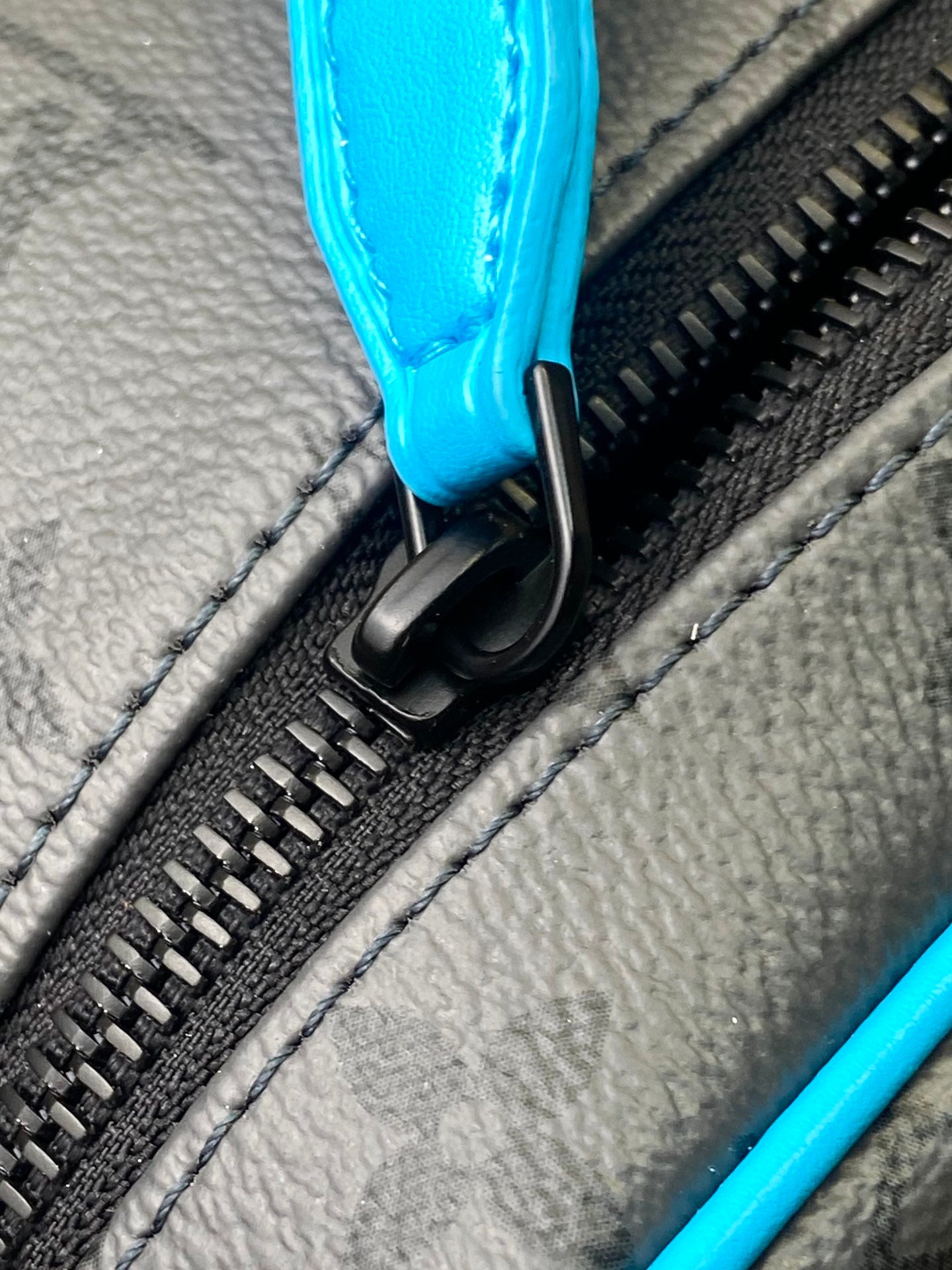 Louis Vuitton zipper pull close-up with black hardware and bright blue leather tab