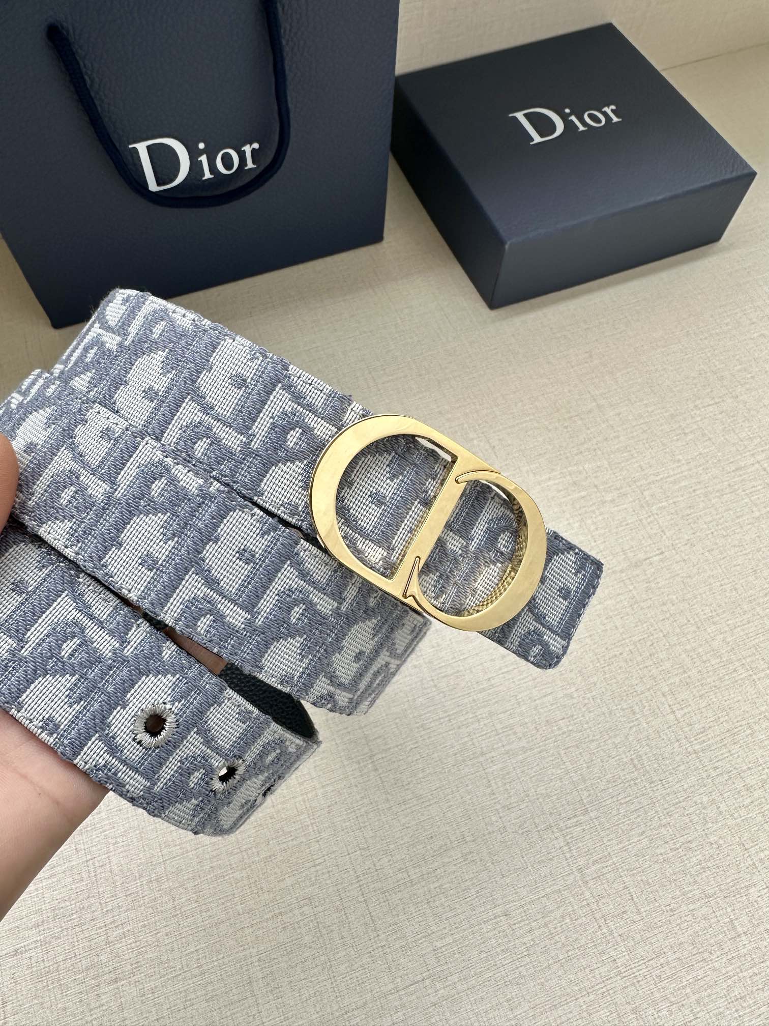 Dior belt close-up with light blue monogram strap and gold-tone oval buckle