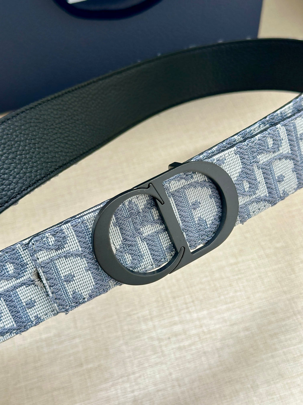 Monogram belt buckle detail on blue-gray patterned strap with leather edge