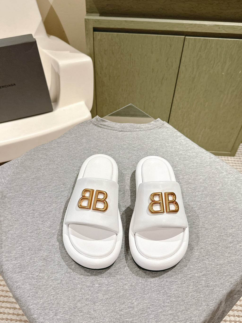 White Balenciaga slide sandals with gold “BB” logo on front straps