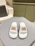 White Balenciaga slide sandals with gold “BB” logo on front straps