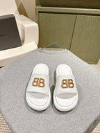White Balenciaga slide sandals with gold “BB” logo on front straps