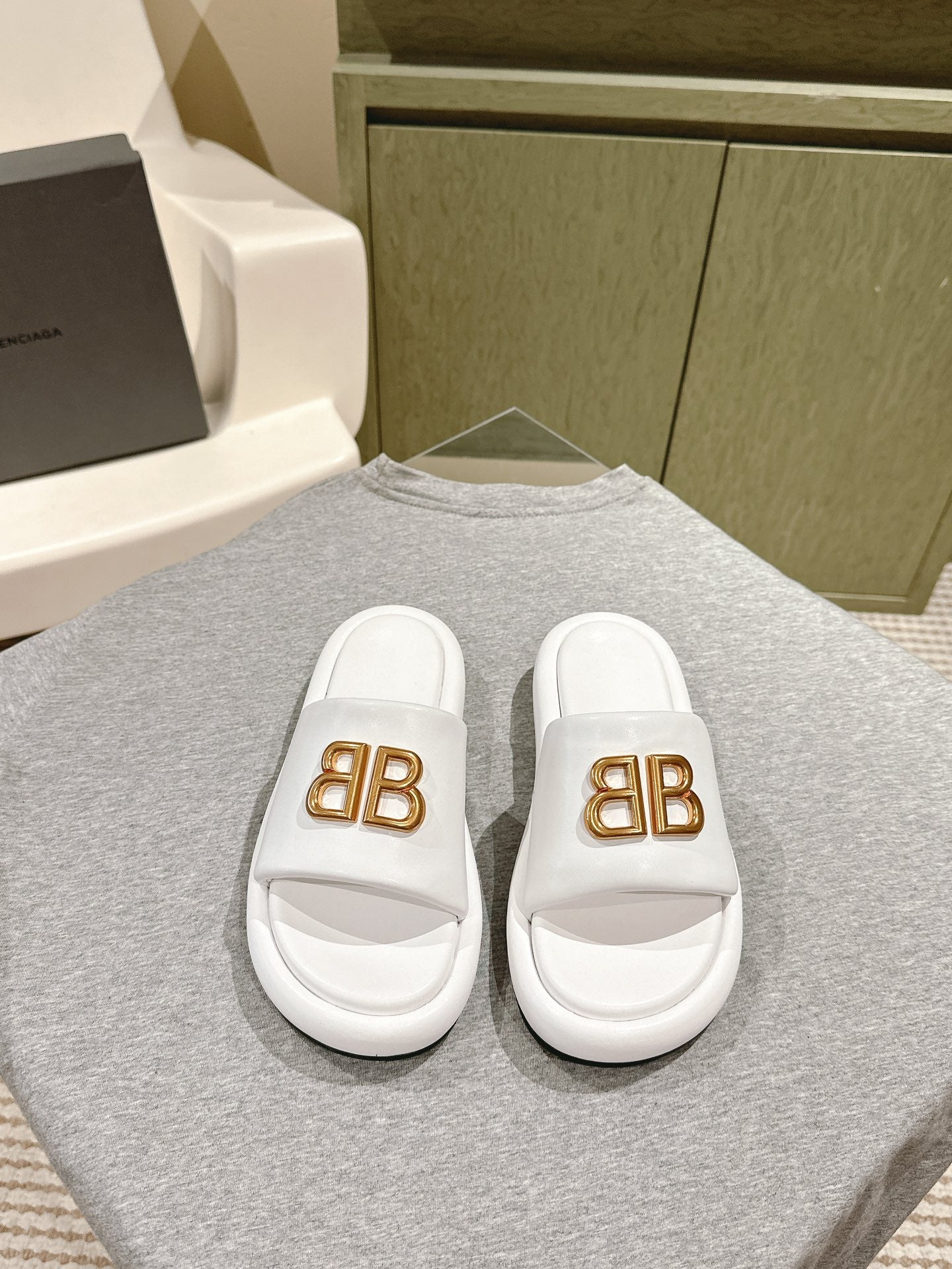White Balenciaga slide sandals with gold “BB” logo on front straps