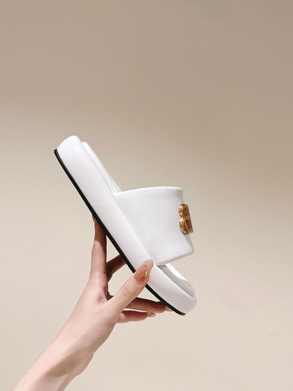 Single white Balenciaga slide sandal held up, showing black sole edge