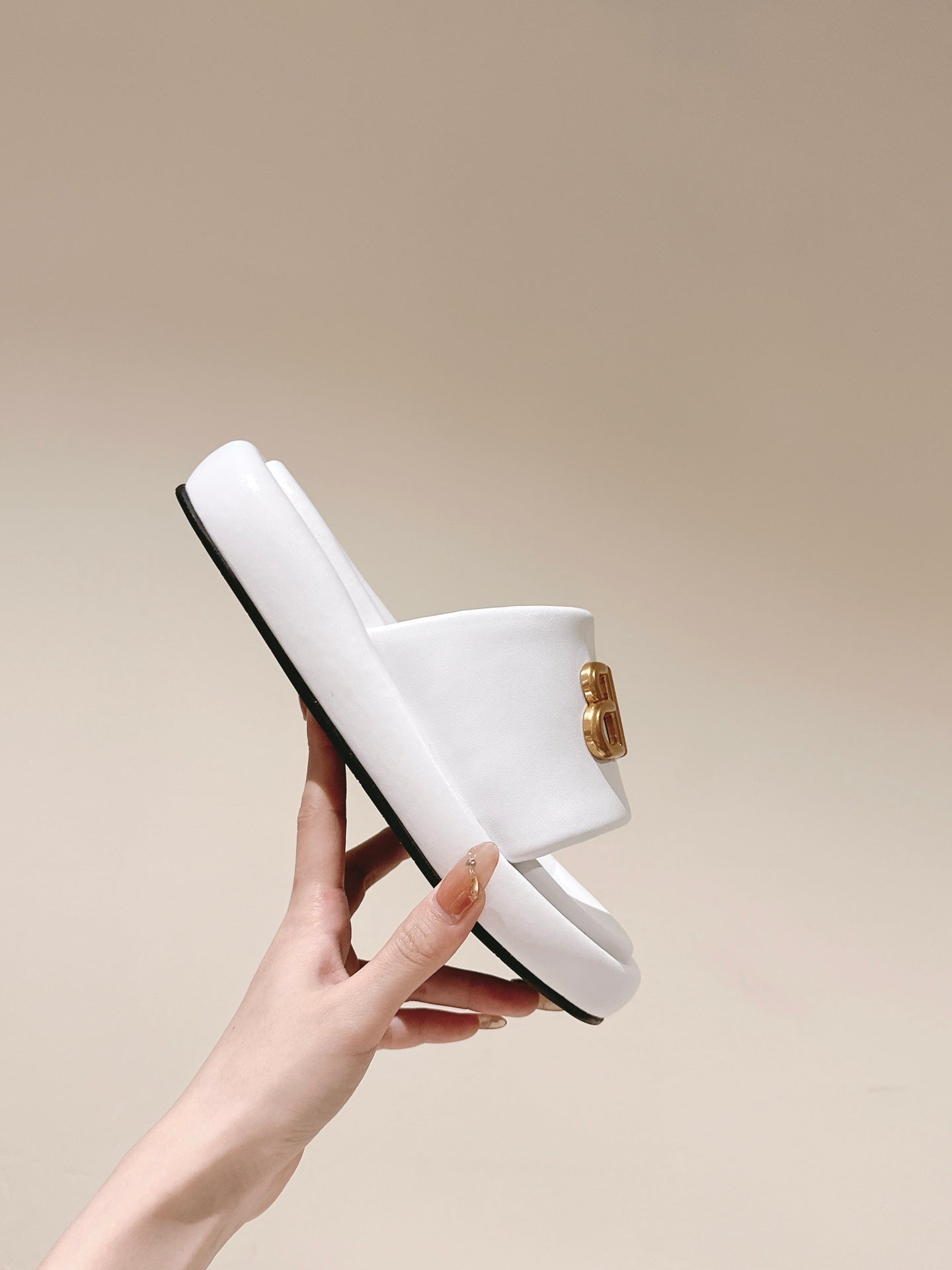 Single white Balenciaga slide sandal held up, showing black sole edge