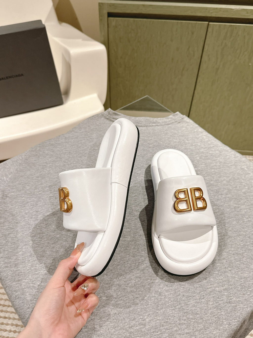 White Balenciaga slide sandals with gold “BB” logo, angled side view