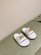 Pair of white Balenciaga slide sandals with gold “BB” logo on straps